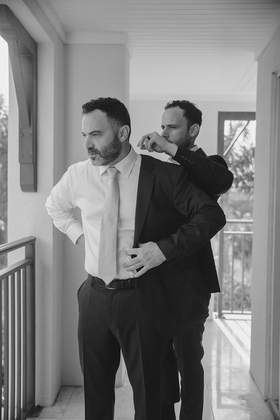 Groom putting on his jacket with help from a groomsman
