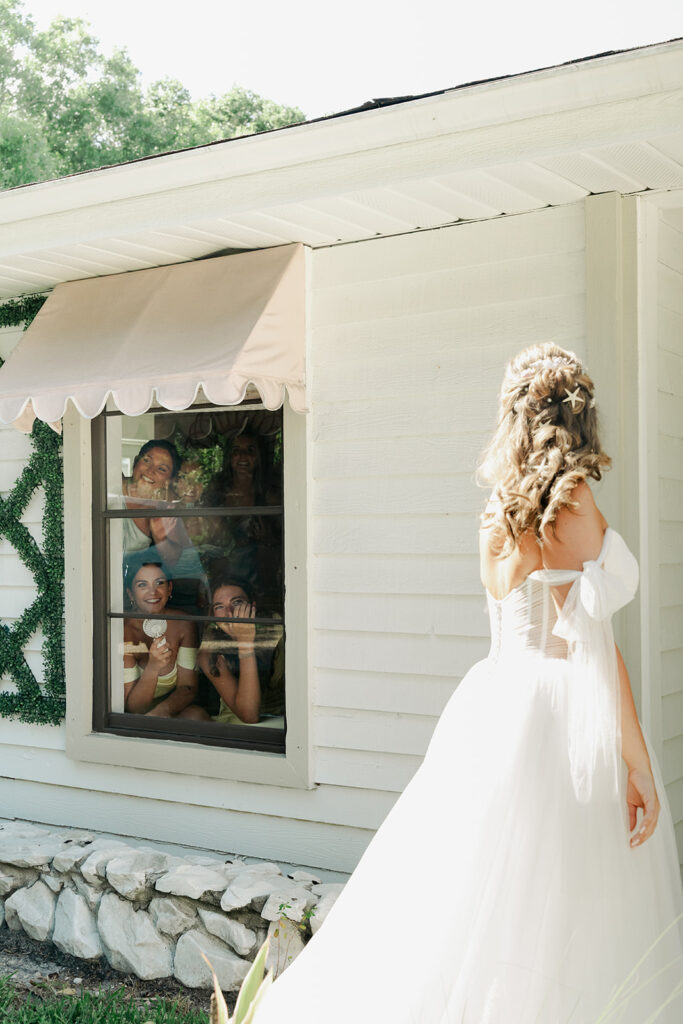 Bridesmaids smiling through a window at the bride