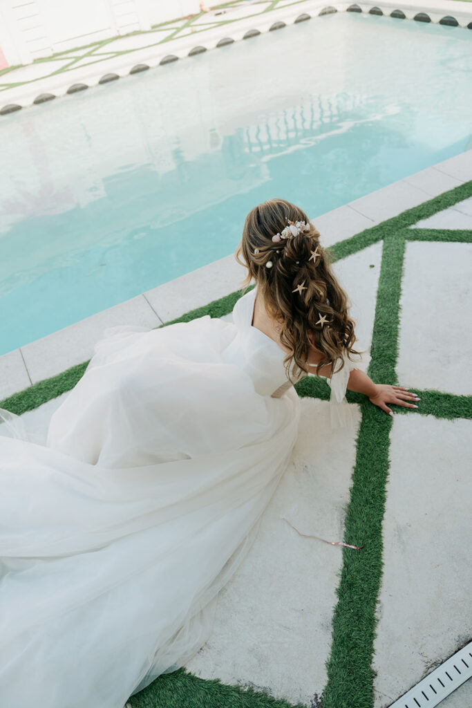 Bride seated beside the pool, showing her wedding hairstyle and dress
